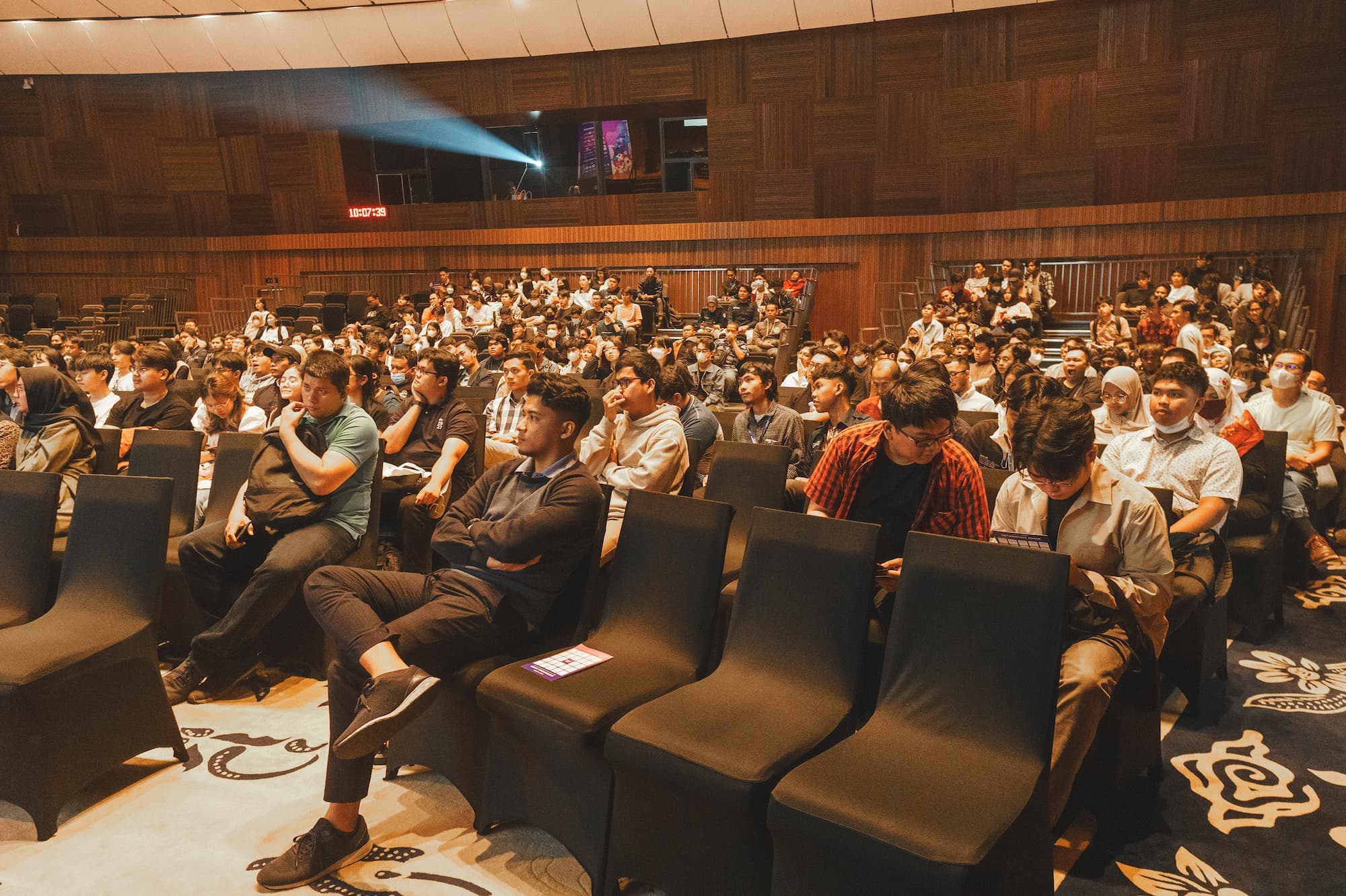 Audience seated in a large auditorium, attentively watching a presentation.